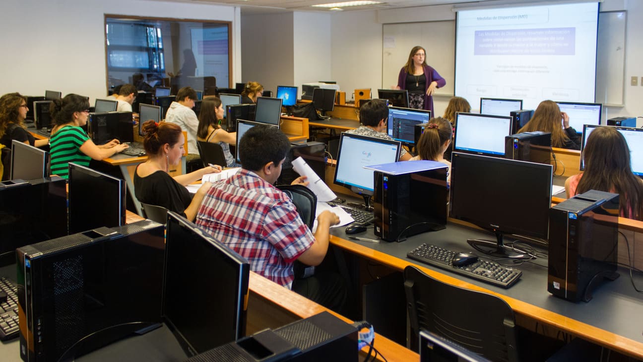 Alumnos en la sala de computación prestando atención a profesora